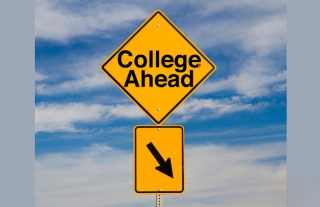 Yellow road sign with the words "College Ahead" and a downward arrow, set against a blue sky with clouds.